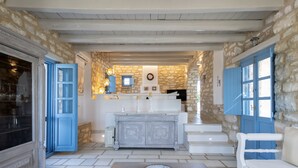 A stone-walled room with a white bench, a white sofa, and a central white cabinet with blue doors. - Sand Key Villa 1 - A beautiful cycladic residence 400m from the beach (Paros)