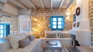 A cozy living room with a stone wall, a white sofa, a wooden table, and a fireplace. - Sand Key Villa 1 - A beautiful cycladic residence 400m from the beach (Paros)