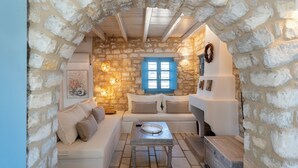 A cozy room with a stone wall, a blue-framed window, a white sofa, and a small table. - Sand Key Villa 1 - A beautiful cycladic residence 400m from the beach (Paros)