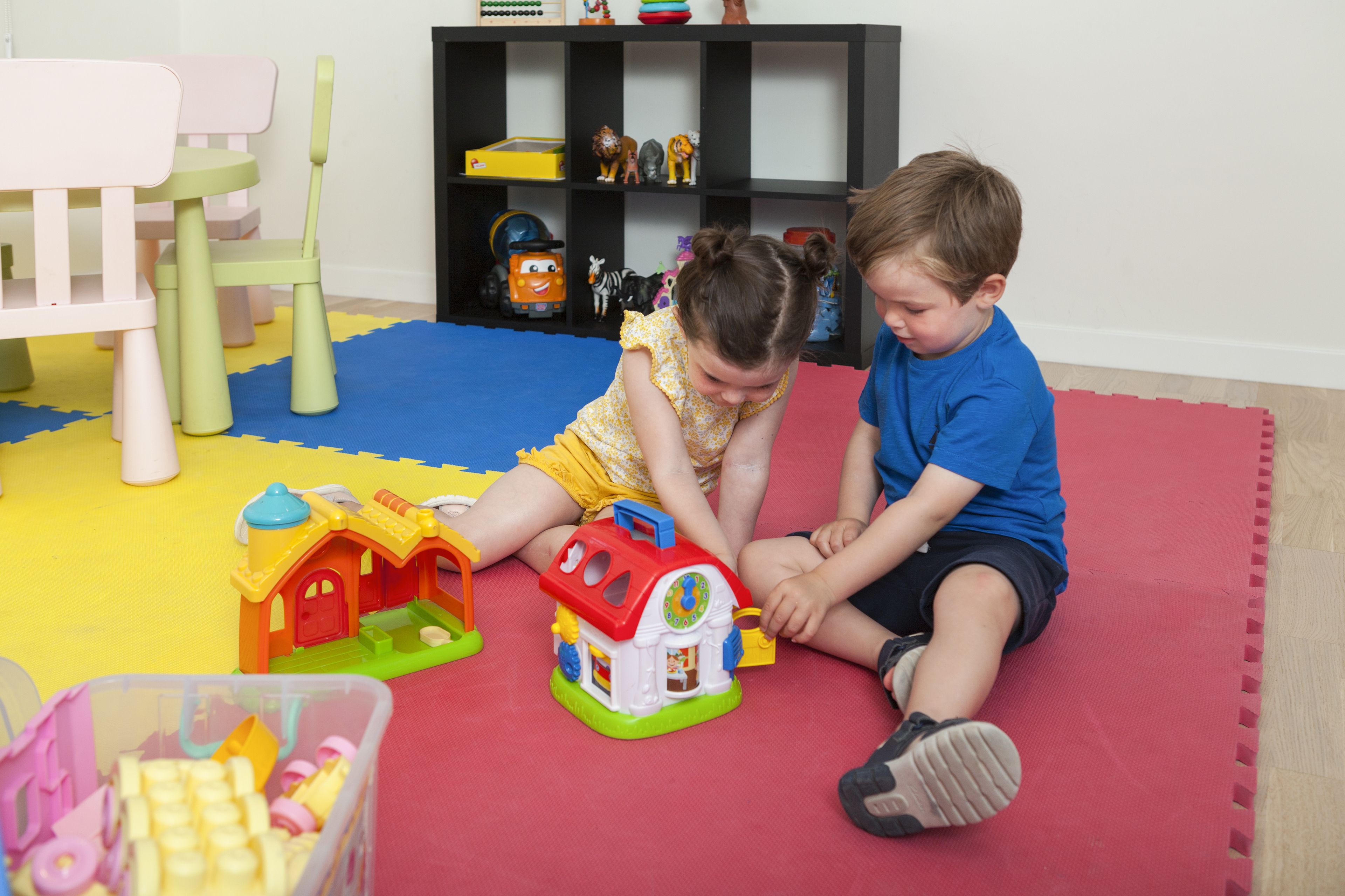 Zwei Kinder spielen mit Spielzeugautos auf einer bunten Spieldecke.