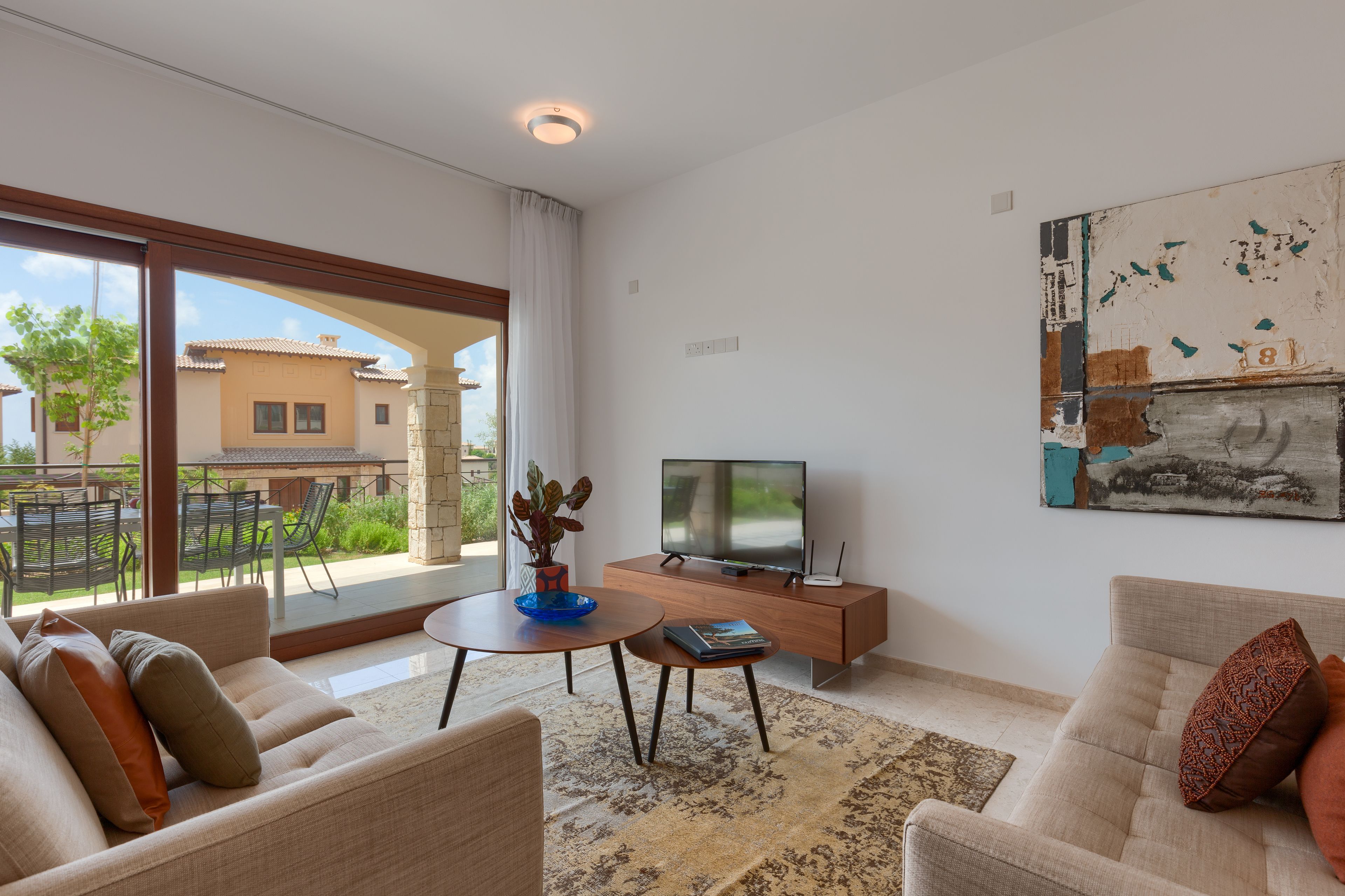 A modern living room with a large TV, comfortable seating, a coffee table, and a view of the outside.