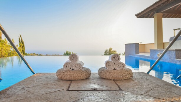 Zona de piscina con dos cestas tejidas que contienen toallas enrolladas, vista despejada a la piscina y una extensión acuática tranquila al fondo.
