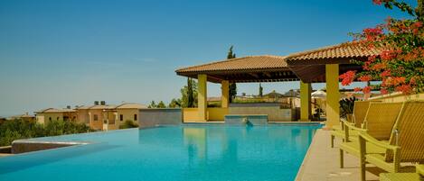 A clear blue swimming pool with a pergola and lounge chairs, surrounded by buildings.