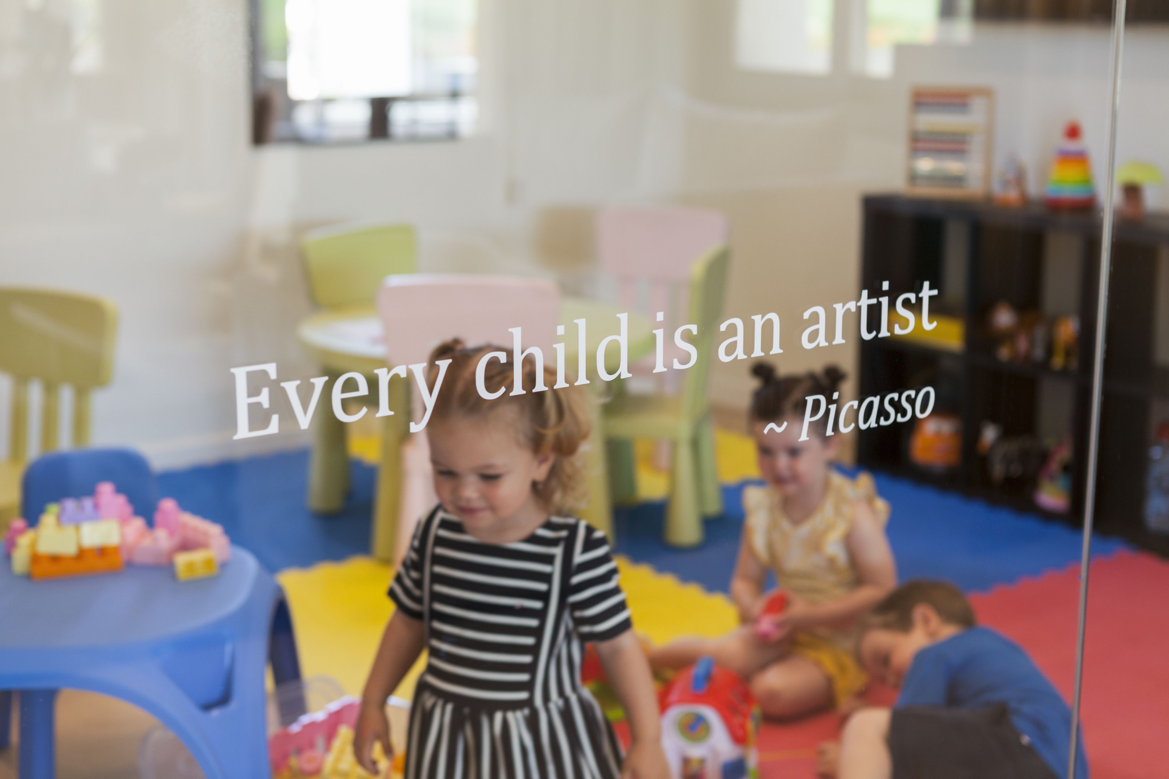 A child in a striped dress playing with toys in a brightly lit room with colorful chairs and tables.