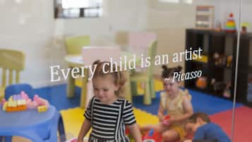A child in a striped dress playing with toys in a brightly lit room with colorful chairs and tables.