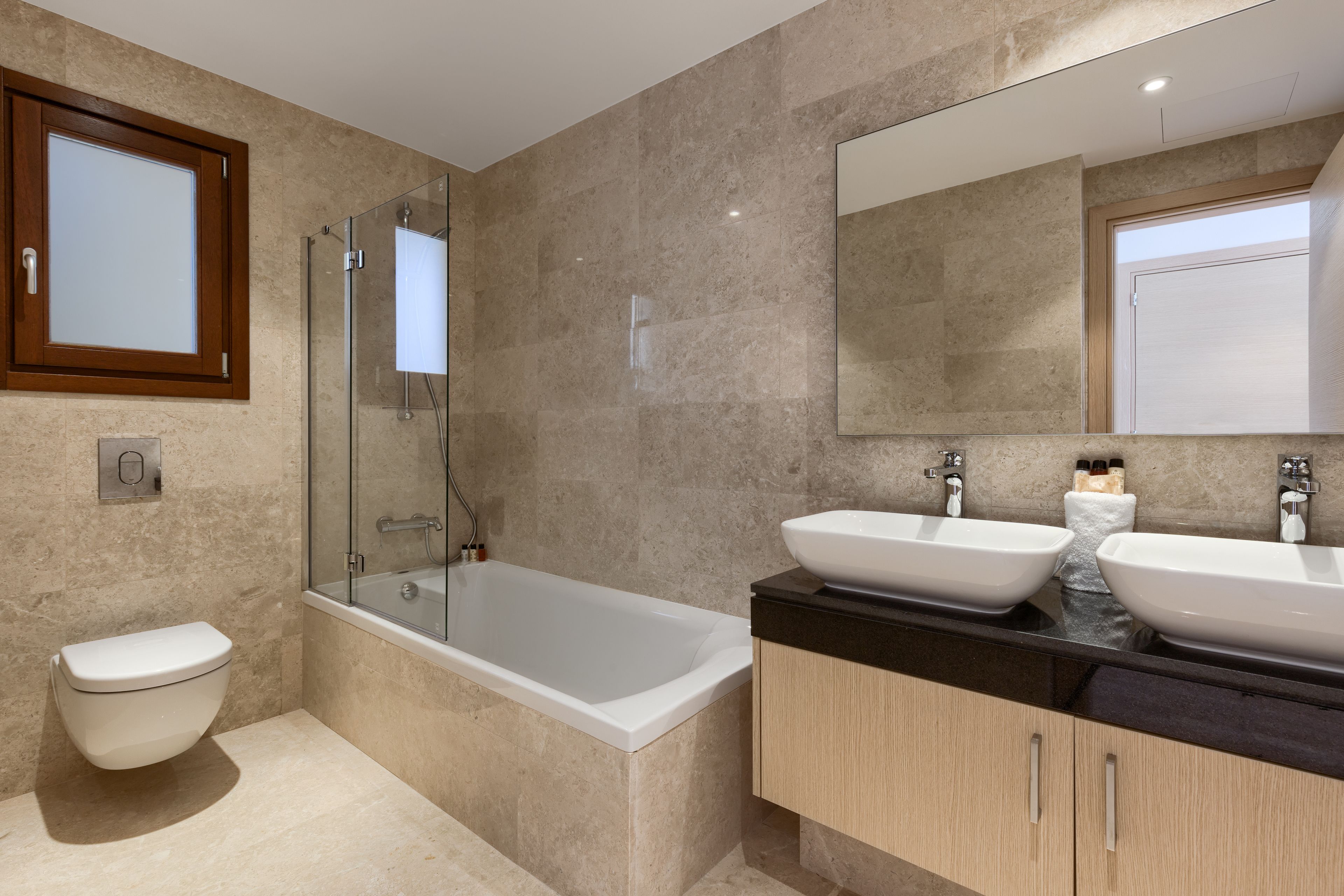 Un baño moderno con bañera, dos lavabos, inodoro y cabina de ducha con mampara de vidrio.