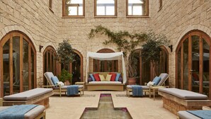 Un patio con muro de piedra, ventanas arqueadas, zona de estar central con cojines y sillones de relax.