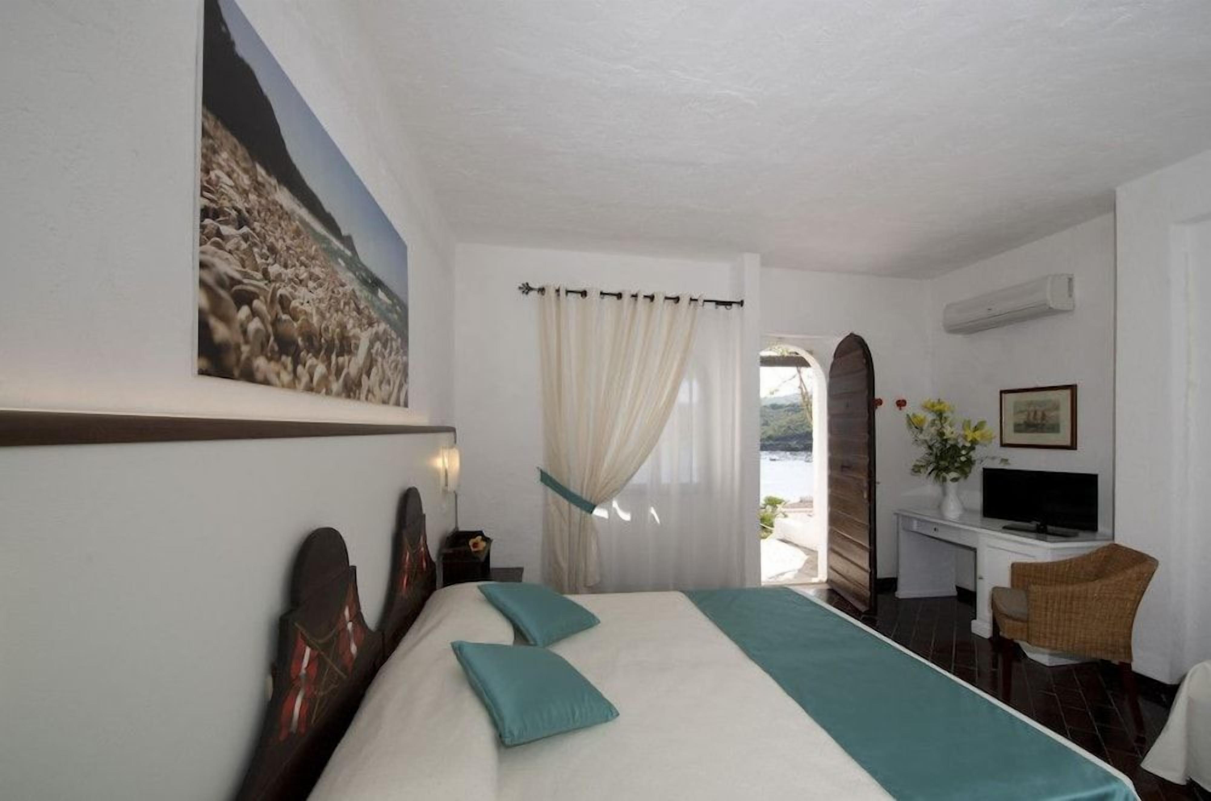 A hotel room with a bed, a desk, a chair, a TV, and a painting on the wall.