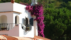 Ein weißes Gebäude mit einem Glockenturm, Terrakottatöpfen mit Blumen und einem Schild mit der Aufschrift 'HOTEL SIBGEN'.