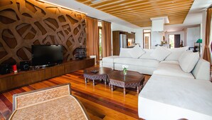 Una sala moderna con techo de madera, un sofá blanco grande, dos mesas de centro de madera y un televisor de pantalla plana sobre un mueble de madera.