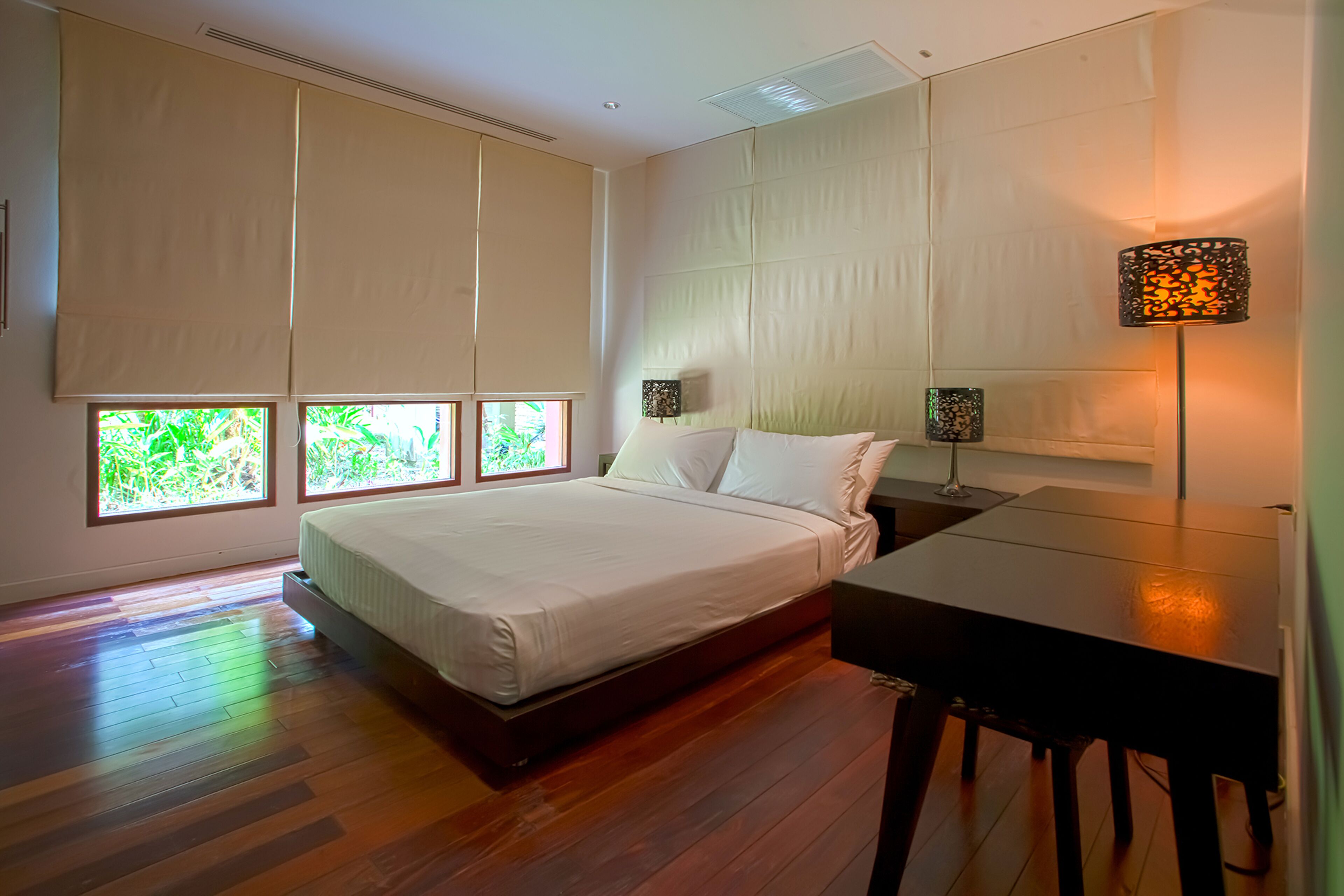 A modern bedroom with a large bed, a desk, and a lamp.