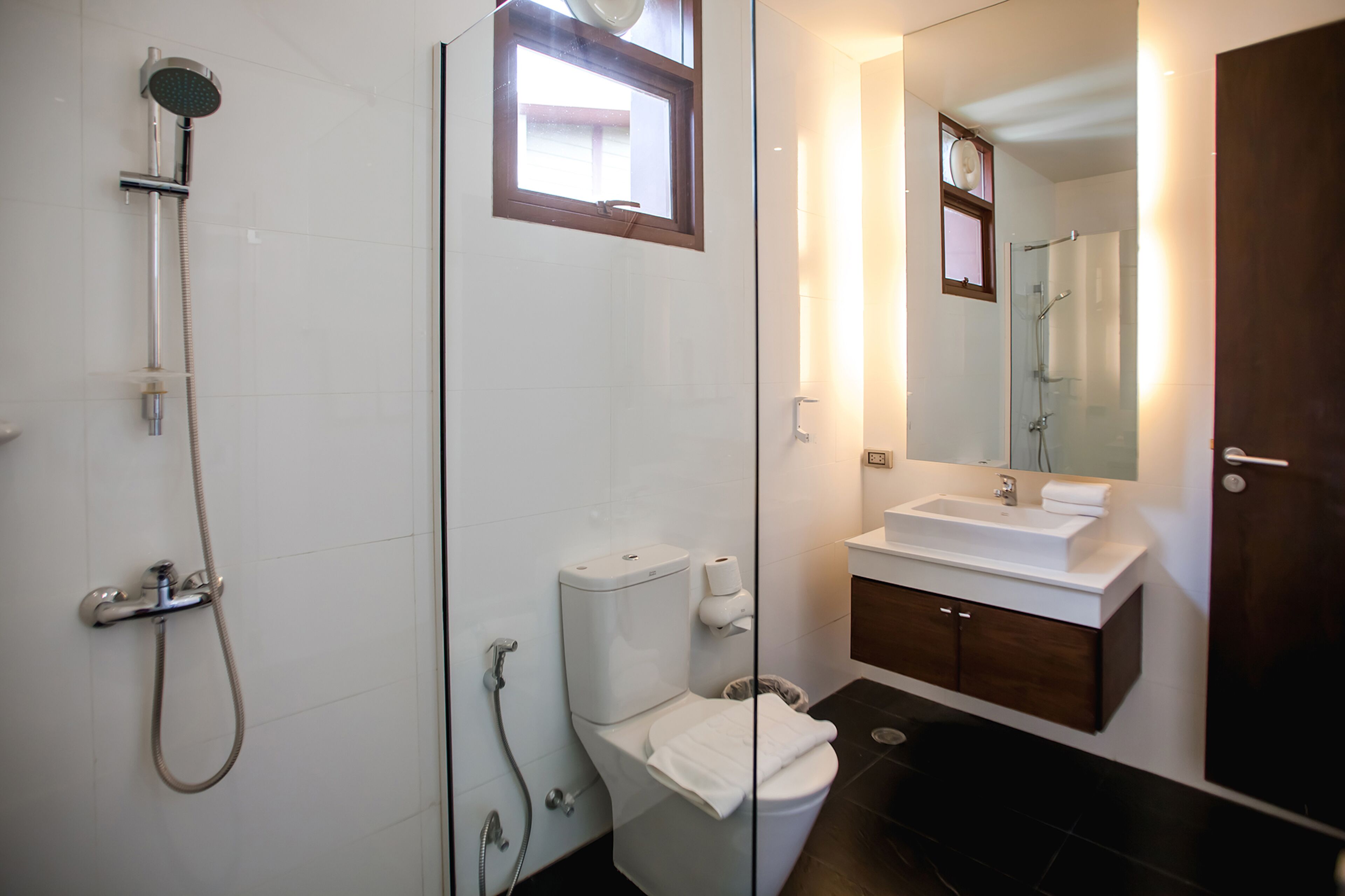 A modern bathroom with a glass shower enclosure, a white toilet, a sink with a mirror, and dark tiled flooring.
