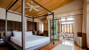 Un dormitorio amplio con cama con dosel, ventilador de techo y vistas al exterior a través de amplias ventanas.