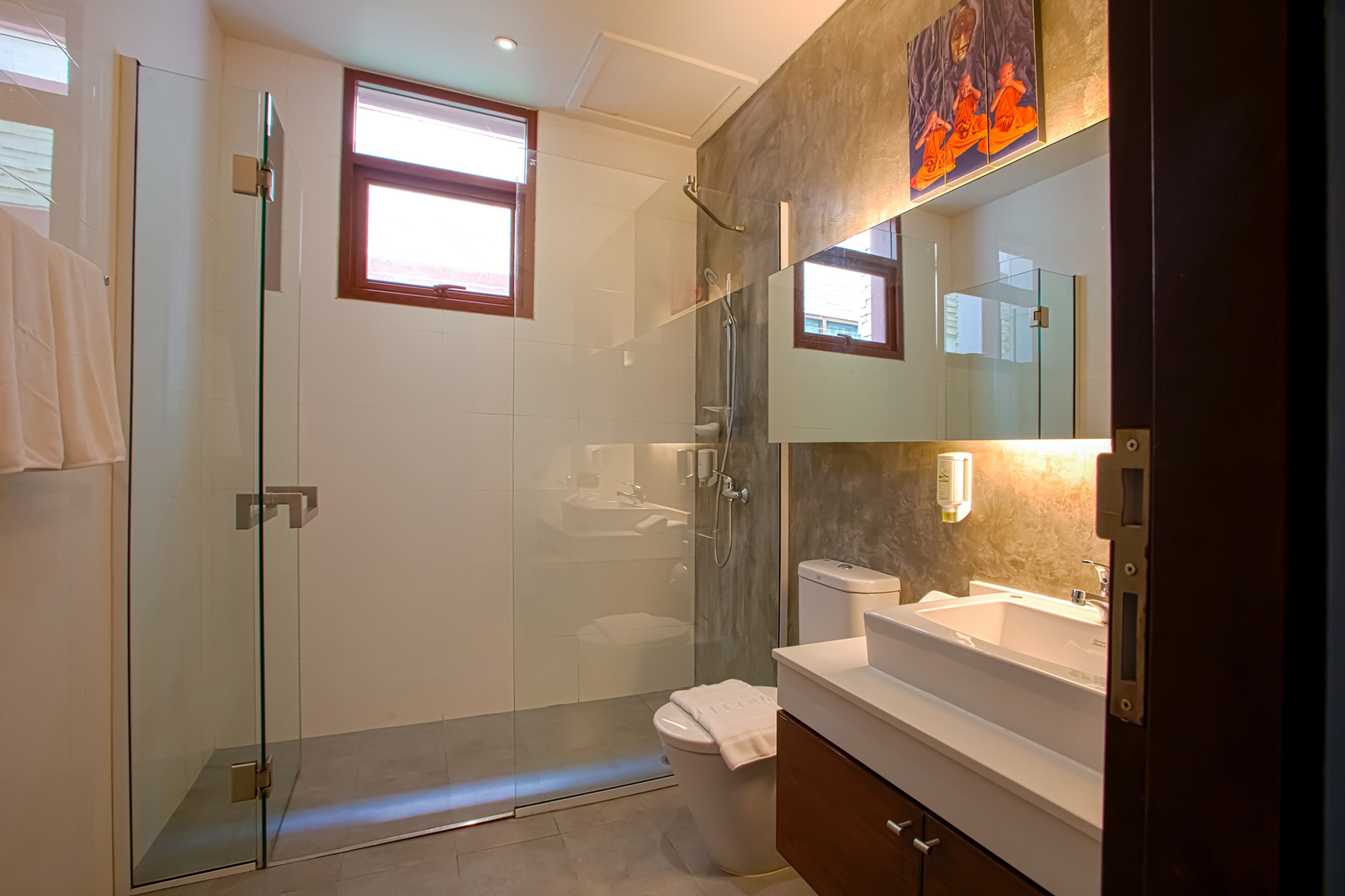 A modern bathroom with a glass-enclosed shower, a white toilet, a vanity with a mirror, and a window providing natural light.