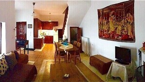 Ein Wohnzimmer mit einer Couch, einem Esstisch und Stühlen. Im Hintergrund ist eine Küche zu sehen.