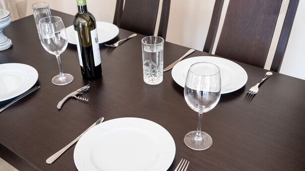 A dining table set with plates, cutlery, wine glasses, and a bottle of wine. - Stunning Maisonette close to the sea with breathtaking view and pool (Πόρτο Χέλι)