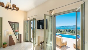A modern hotel room with a glass door leading to a balcony with a pool view. - Stunning Maisonette close to the sea with breathtaking view and pool (Πόρτο Χέλι)