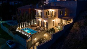 A two-story house with a swimming pool, outdoor seating, and a stone wall. - Stunning Maisonette close to the sea with breathtaking view and pool (Πόρτο Χέλι)