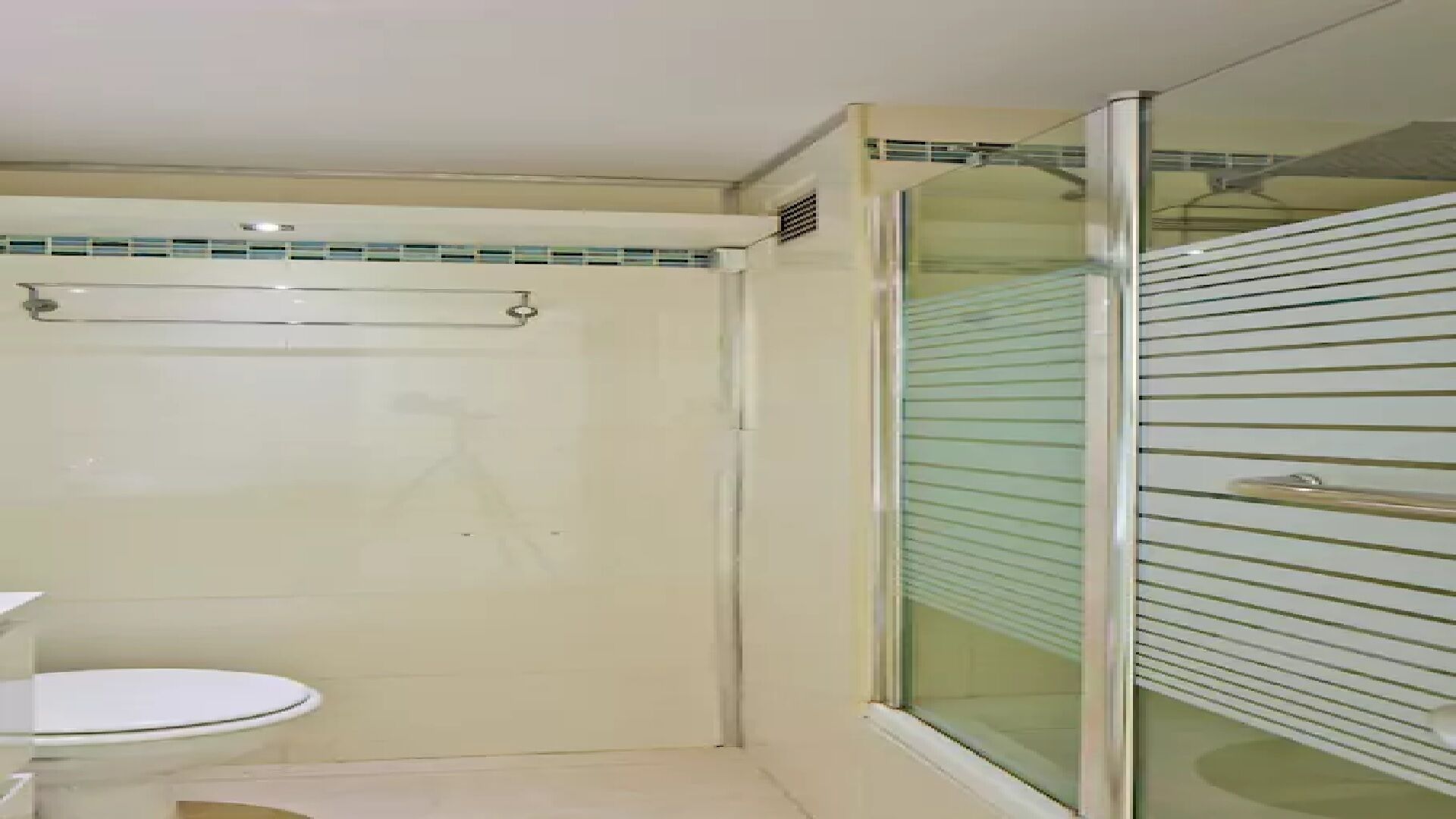 A bathroom with a glass shower enclosure, a toilet, and a sink.