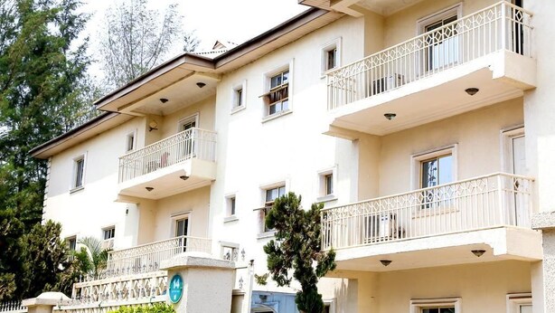 A multi-story hotel with balconies, a central entrance, and a surrounding fence. - Barcelona Apartment (Abuja)