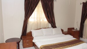A bedroom with a bed, wooden nightstands, a desk, and curtains. - Barcelona Apartment (Abuja)