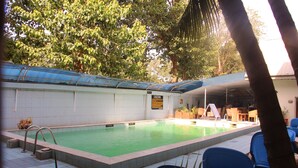 A swimming pool with a blue roof, surrounded by chairs and potted plants. - Barcelona Apartment (Abuja)