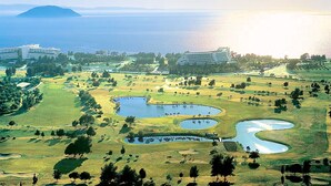 Camp de golf amb diversos estanys, envoltat d'edificis i vistes a l'oceà.