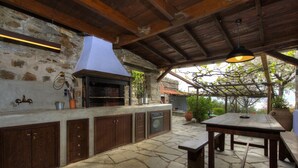 Cuina exterior amb paviment de pedra, armaris de fusta i forn integrat.