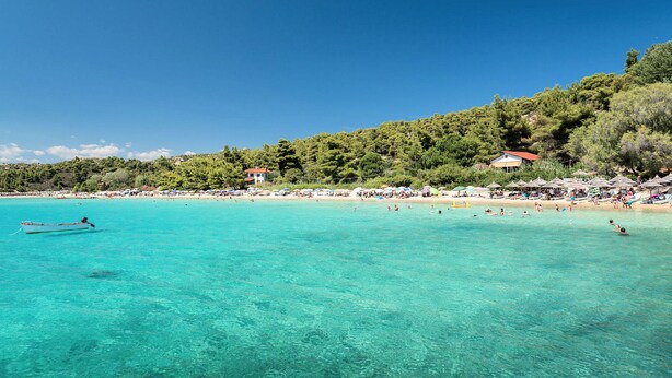 Una platja amb aigua turquesa cristal·lina, un vaixell i sombrerelles de platja.