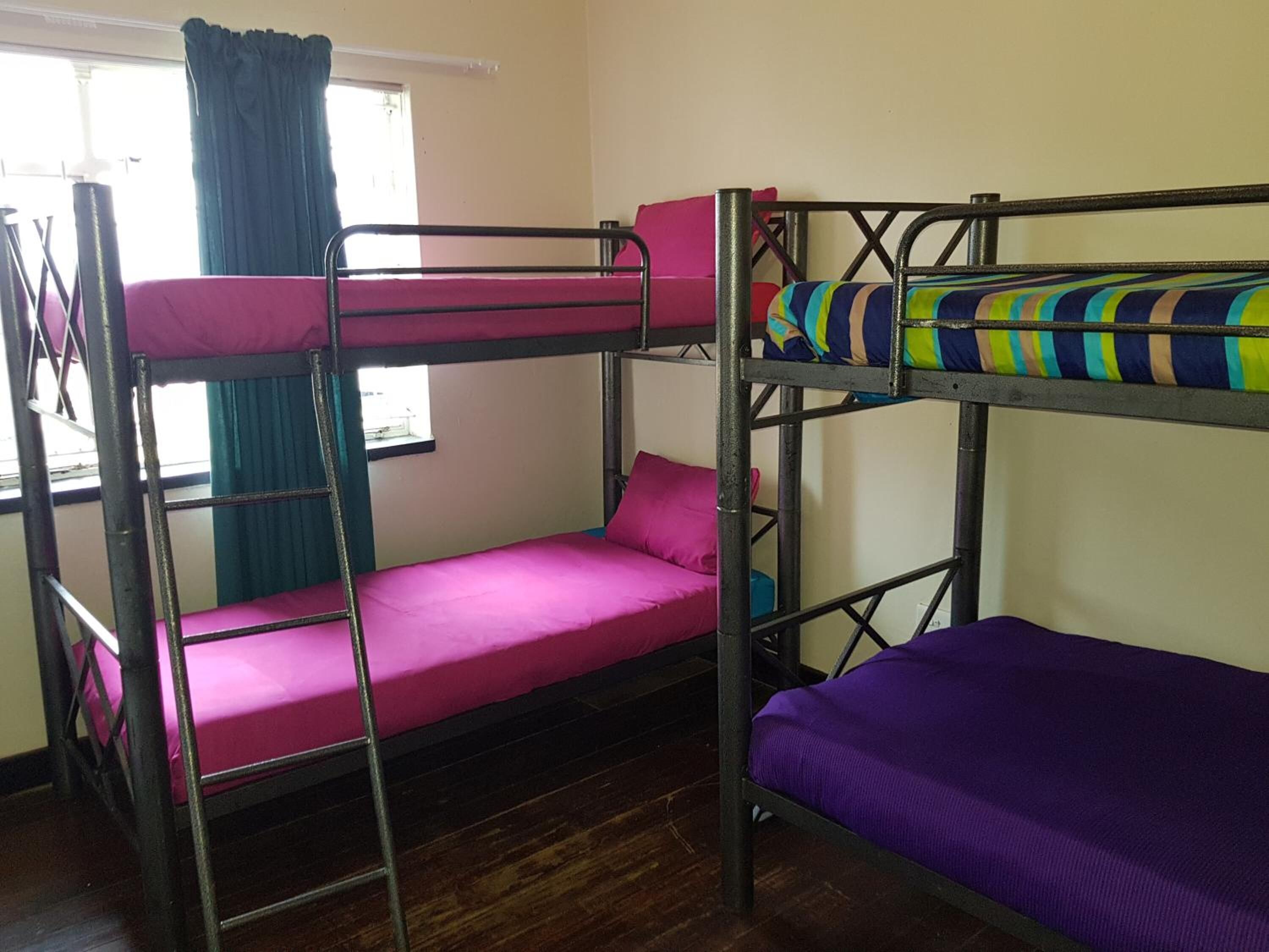 A bunk bed room with two beds, one on top of the other, and a window with curtains.