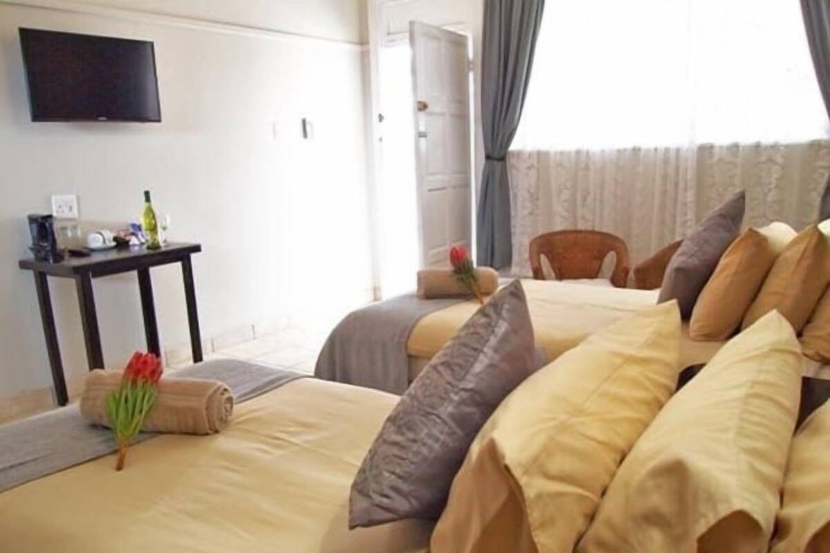 A hotel room with two beds, a TV mounted on the wall, a small table with a bottle and a glass, and a window with curtains.