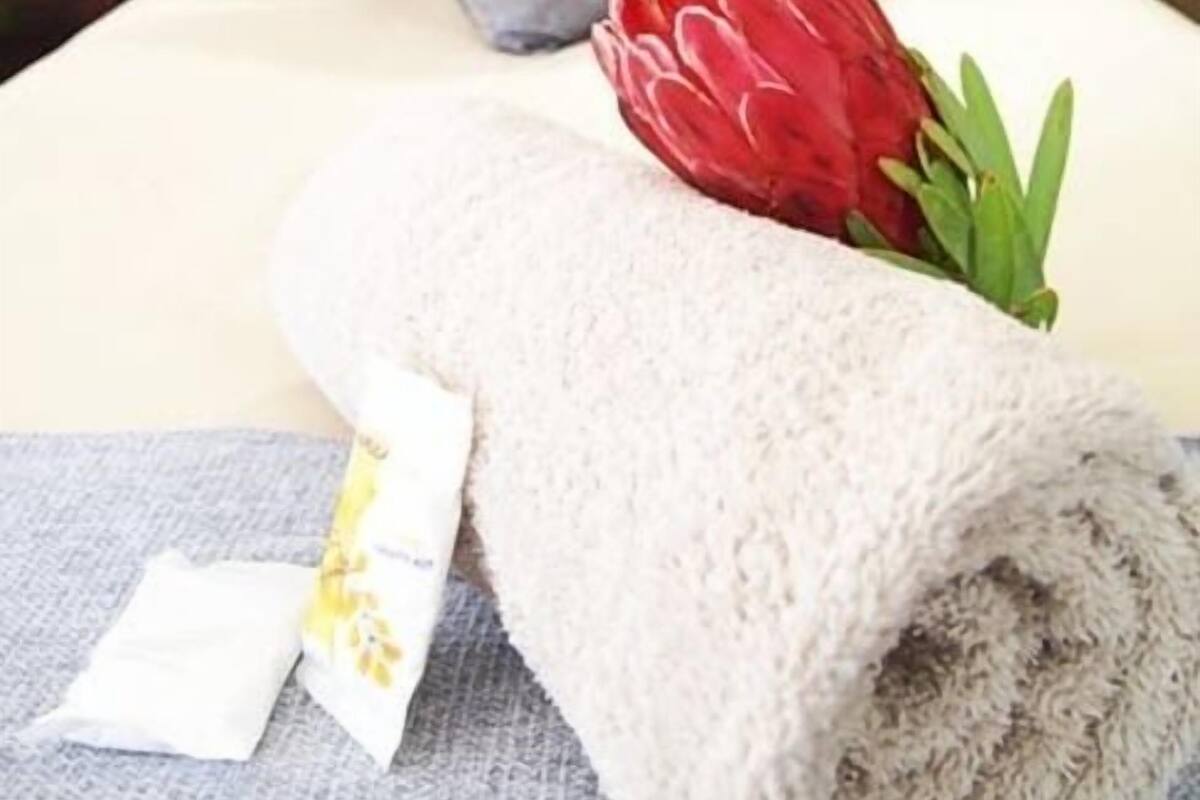 A neatly made bed with a grey pillow, a red flower, and a rolled towel.