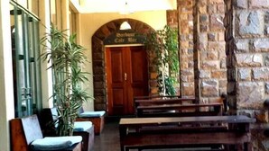 A lobby with a stone wall, wooden benches, a reception desk, and a sign for Harbour Cafe Bar. - Travel Lodge Sabie (Sabie)
