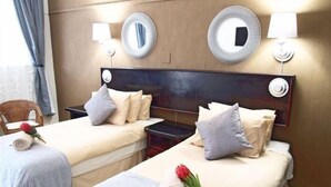 A hotel room with two beds, each with a pillow and a rolled towel. There are two wall-mounted lamps and two mirrors. A chair and a red flower are also visible. - Travel Lodge Sabie (Sabie)
