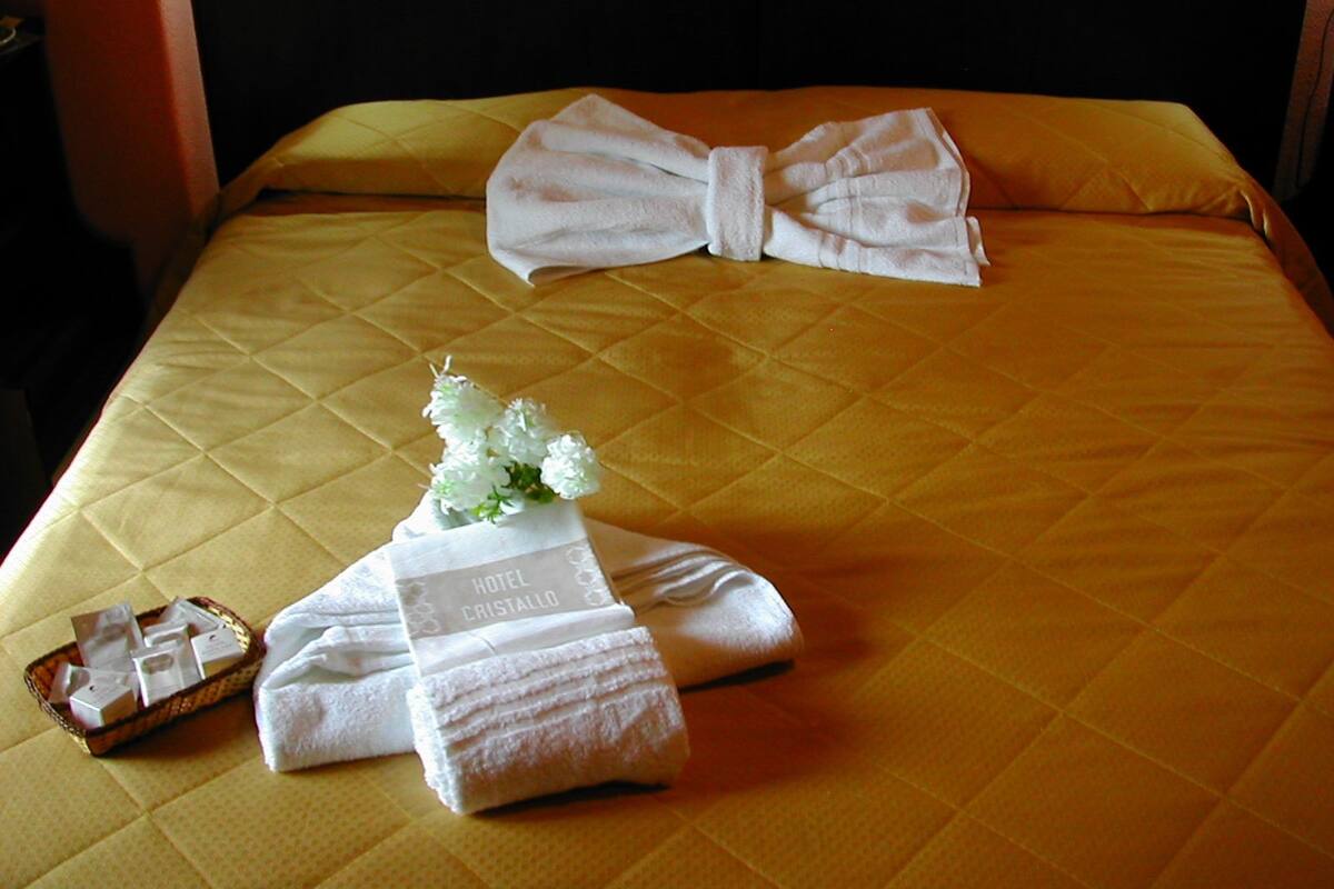 Un lit bien fait, recouvert d’une couvre-lit jaune, un bouquet de fleurs blanches et un panier rempli de produits de toilette.
