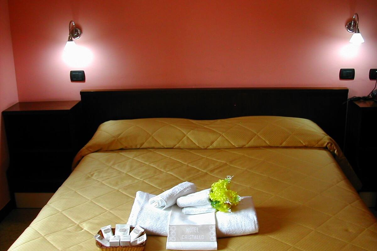 Une chambre d’hôtel avec un lit, deux lampes de chevet, une table de chevet et un panier contenant des articles de toilette.