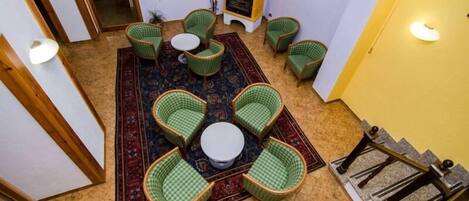 A cozy room with a central round table surrounded by four green checkered chairs, a patterned rug, and a wood-burning stove.