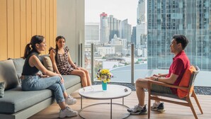 Ein modernes Interieur mit einer Couch und Sesseln vor einem großen Fenster mit Blick auf eine Stadtlandschaft.