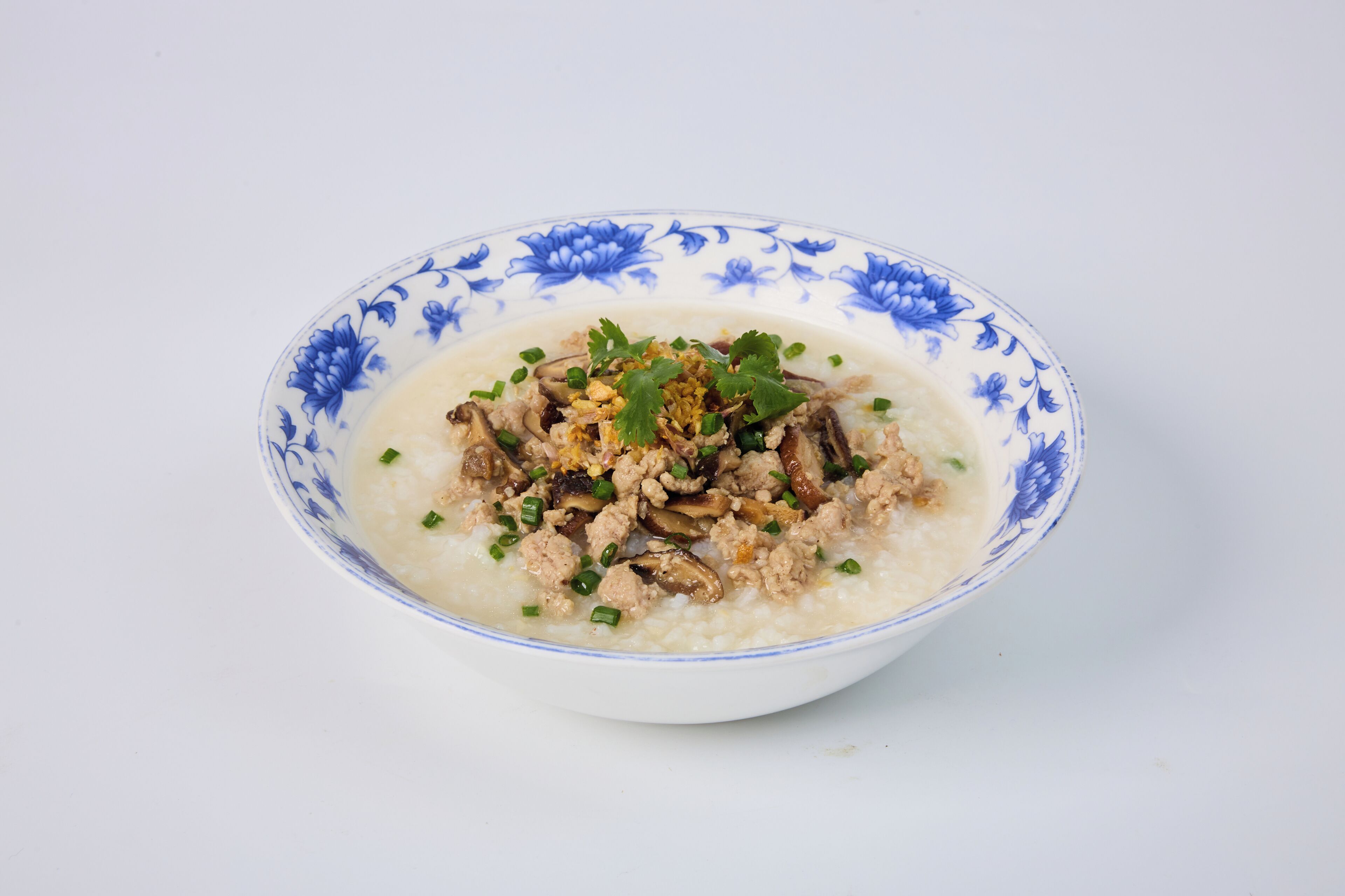 A bowl of rice porridge with meat and green onions.