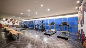 Ein Fitnessraum mit Trainingsgeräten, Holzboden und großen Fenstern mit Blick auf die Stadt.