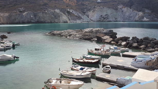 Un port de plaisance avec des bateaux amarrés, un terrain rocheux et un petit bâtiment en arrière-plan.