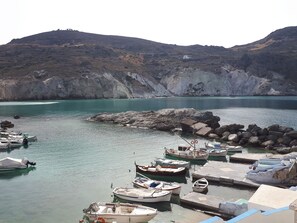 A coastal marina with boats docked, rocky terrain, and a small white building in the background. - "Sea Blue" traditional cycladic residence with sea view terrace (Μανδράκια)
