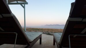 Vue depuis un balcon, avec deux chaises longues donnant sur une plage et des montagnes.