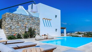 Une villa moderne dotée d’un mur en pierre, d’une piscine et offrant une vue sur la mer.