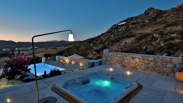 Un bain à remous doté d’un mur en pierre et d’une lampe, offrant une vue sur un paysage montagneux.