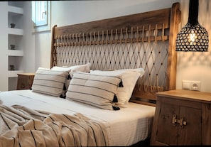 Un lit bien fait, avec des oreillers à rayures, une tête de lit en bois et une table de chevet sur laquelle se trouve une lampe.