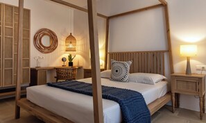 A four-poster bed with a wooden headboard, a round mirror, a small table with a plant, and a wall-mounted lamp.
