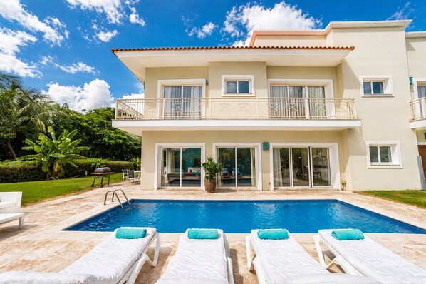 A two-story house with a swimming pool, outdoor seating, and a garden.