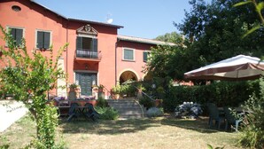 A two-story building with a red facade, a balcony, and a small garden area with outdoor furniture. -  Vigna dell'Agrifoglio Home Residence di Eugenio Azzolini (Velletri)