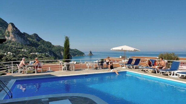Área de piscina com espreguiçadeiras e mesas, com vista panorâmica para as montanhas e o mar.